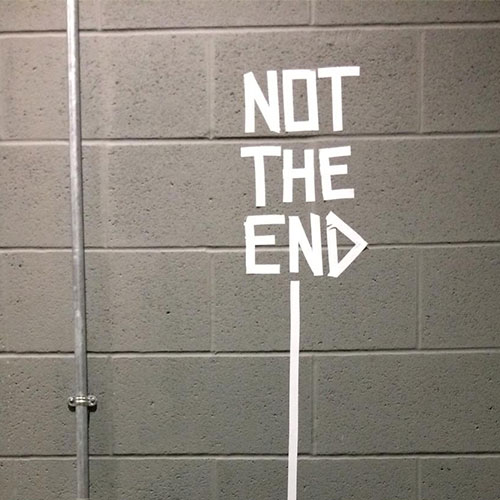 The words It's Not the end in white  taped on a grey brick wall